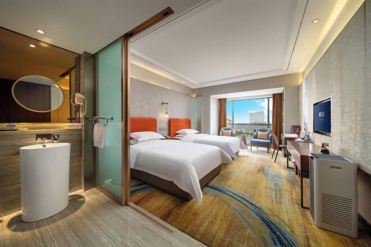Ein Hotelzimmer mit einem großen Bett, einer separaten Sitzecke, einem Fernseher und Blick auf die Stadt.