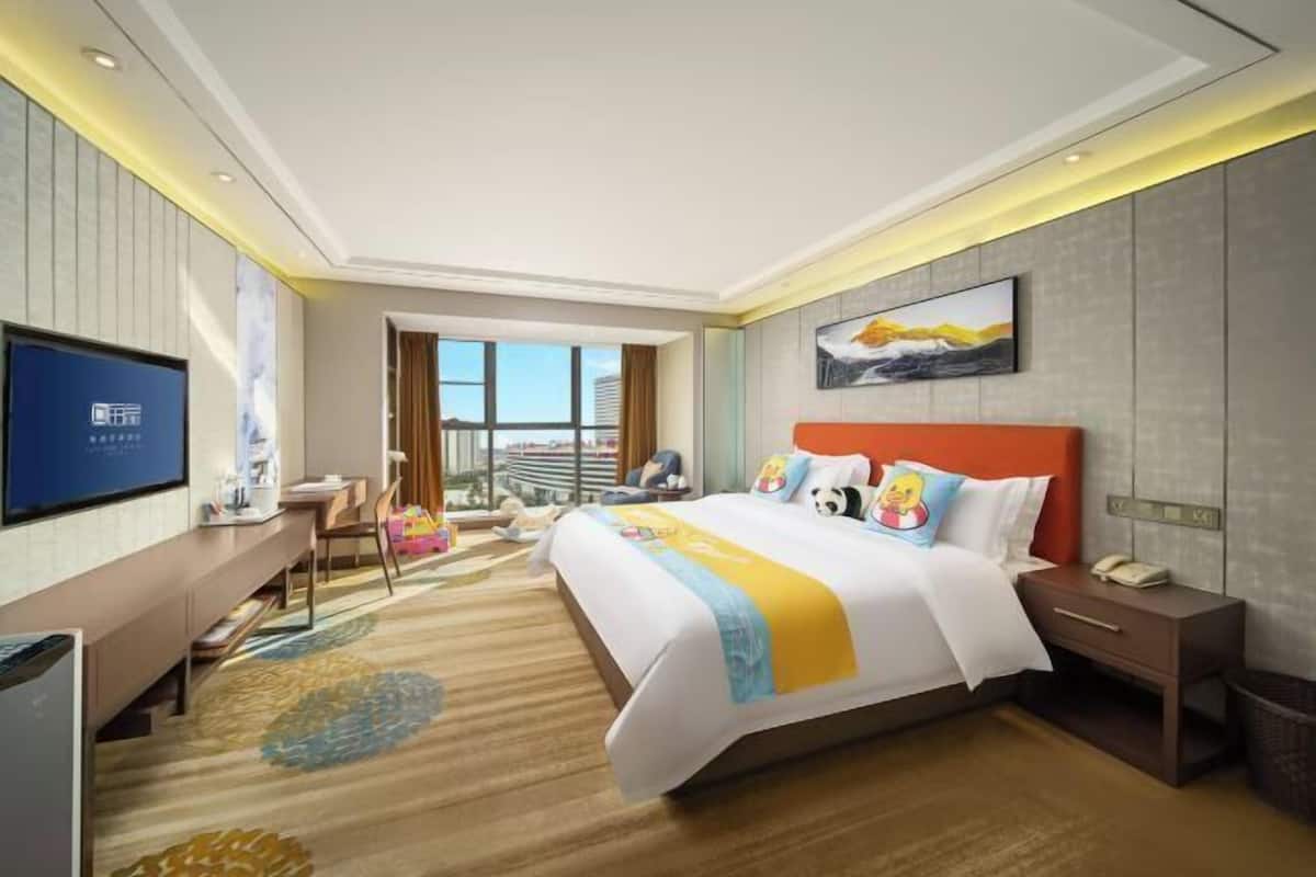 Ein Hotelzimmer mit Bett, Schreibtisch, Fernseher und Fenster mit Blick auf die Stadt.