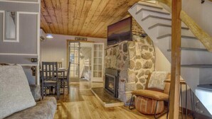 Ein gemütliches Wohnzimmer mit Kamin aus Stein, Holzdielen und einer Treppe, die zu einer oberen Ebene führt.