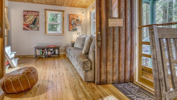 Ein gemütliches Zimmer mit Holzböden, einer Couch, einem Bücherregal und einer Tür, an der ein Schild mit der Aufschrift 'Schuhe ausziehen, bitte' hängt.