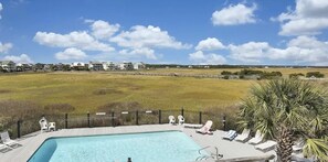 Une piscine avec des chaises longues, donnant sur un champ verdoyant et des bâtiments en arrière-plan.