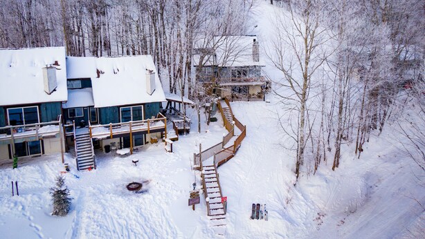 A snow-covered lodge with a deck and outdoor seating, surrounded by trees. - Ski-in ski-out 3 Bdrm Chalet w sauna on slopes & lake - Sleeps 8 (Upson)