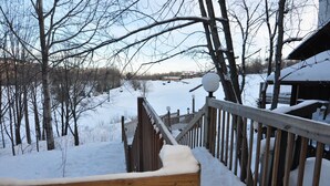 A wooden deck with snow-covered railings overlooking a snowy landscape with bare trees and a distant building. - Ski-in ski-out 3 Bdrm Chalet w sauna on slopes & lake - Sleeps 8 (Upson)