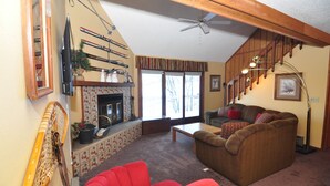A living room with a fireplace, a red armchair, a brown sofa, and a ceiling fan. - Ski-in ski-out 3 Bdrm Chalet w sauna on slopes & lake - Sleeps 8 (Upson)