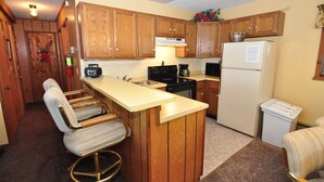 A compact kitchen with wooden cabinets, a built-in bar stool, a refrigerator, and a stove. - Ski-in ski-out 3 Bdrm Chalet w sauna on slopes & lake - Sleeps 8 (Upson)