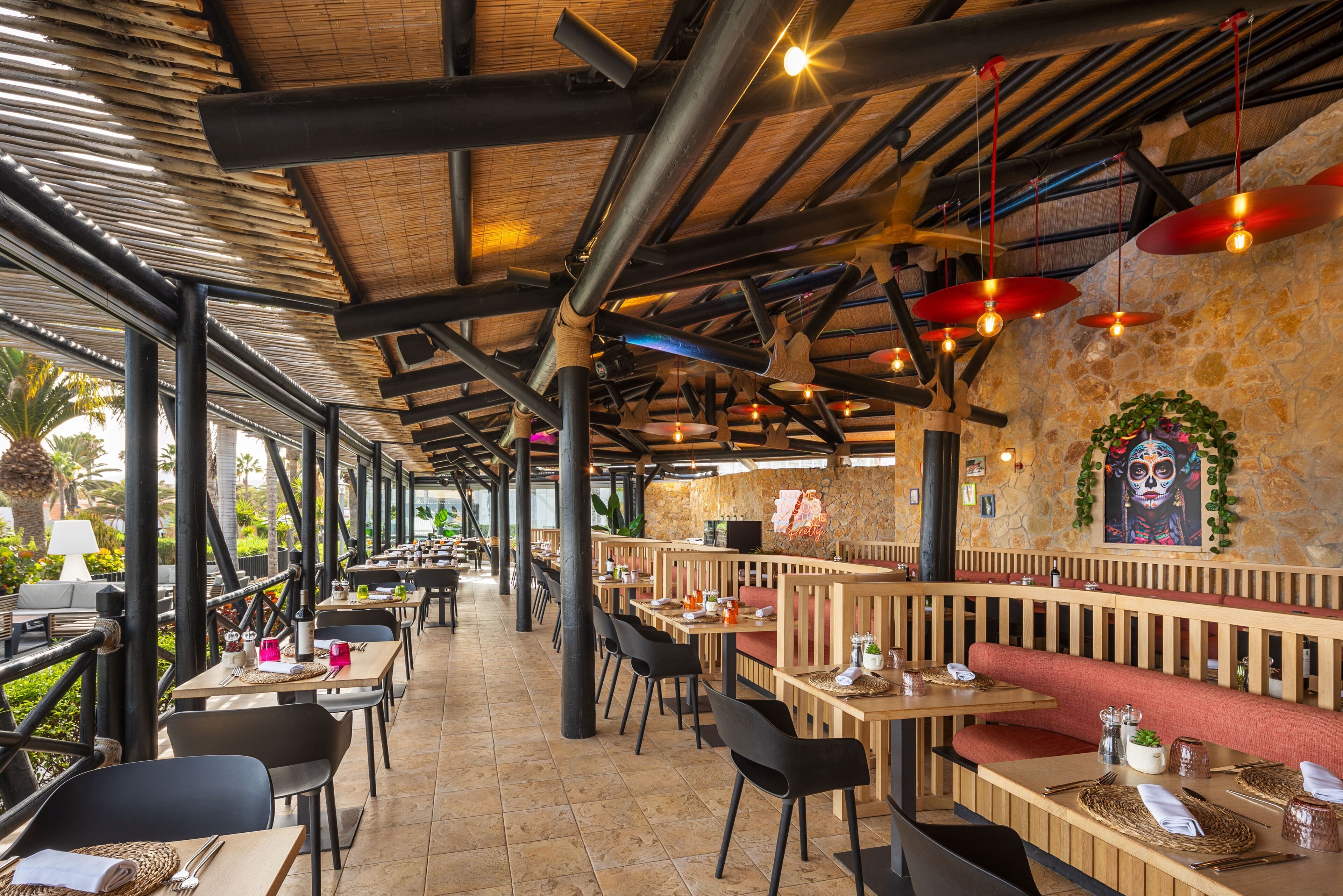 An outdoor restaurant with wooden tables and chairs, stone walls, and hanging red lanterns.