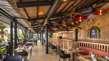 An outdoor restaurant with wooden tables and chairs, stone walls, and hanging red lanterns.