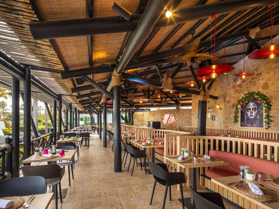 An outdoor restaurant with wooden tables and chairs, stone walls, and hanging red lanterns.