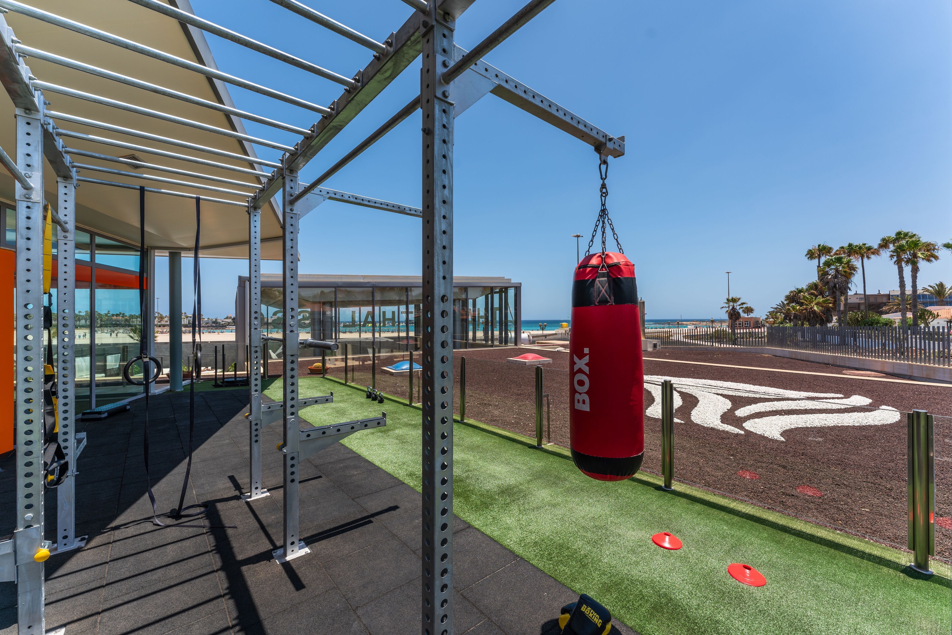 A gym with outdoor exercise equipment, a punching bag, and a clear view of the ocean.
