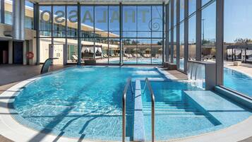 Une piscine intérieure à l’eau d’un bleu limpide, équipée d’une bouée de sauvetage et offrant une vue sur la façade de l’hôtel grâce à de grandes fenêtres.