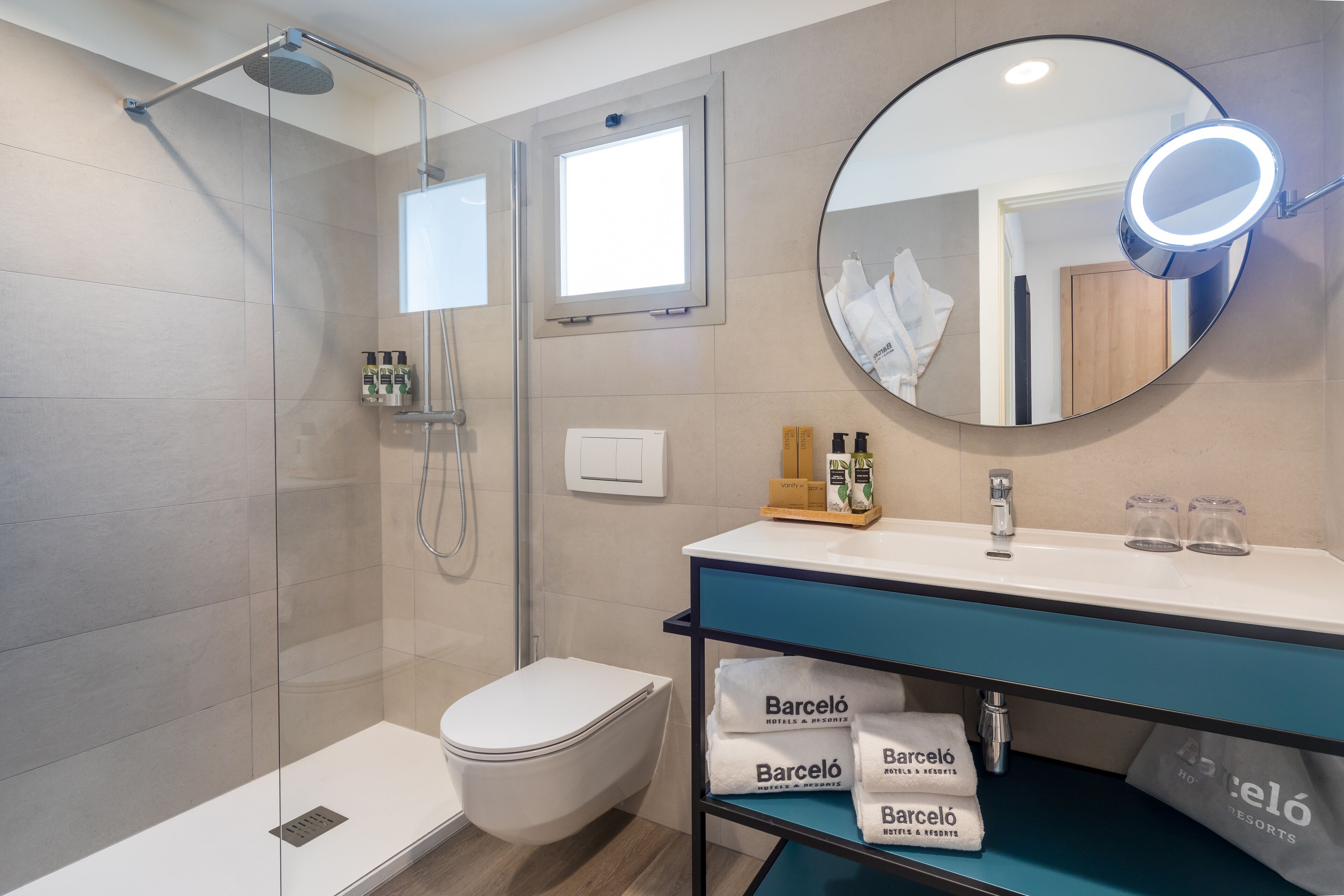 A modern bathroom with a glass-enclosed shower, a toilet, a sink with a mirror, and toiletries on a shelf.