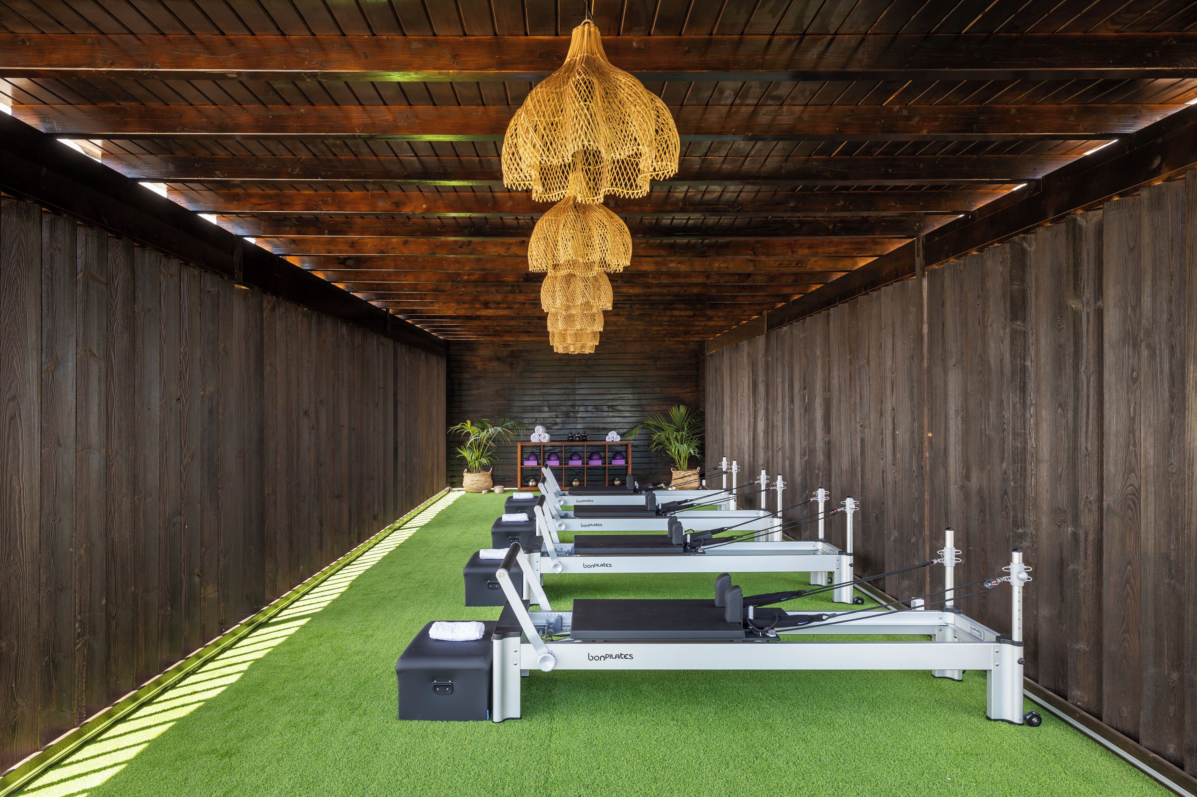 A row of Pilates equipment under a wooden ceiling with a hanging light fixture.