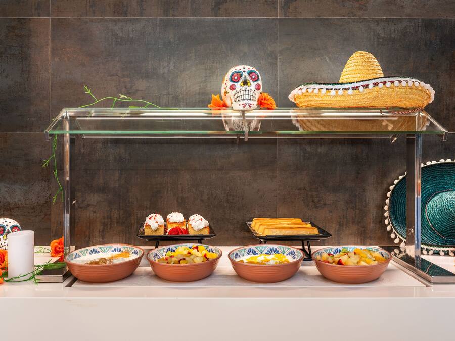 A glass display case with a decorative sombrero, sugar skull, and various desserts.