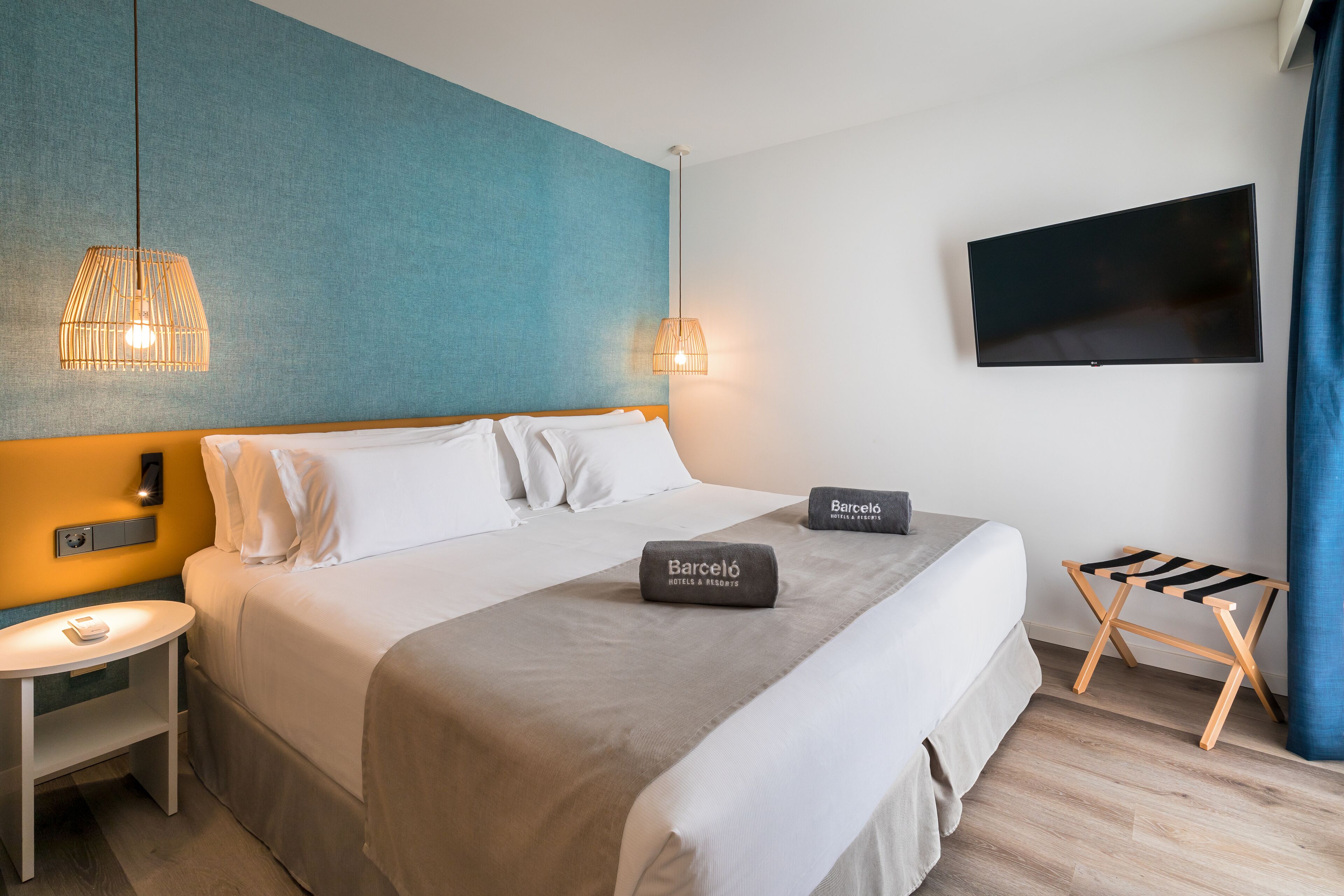 A hotel room with a bed, a nightstand, a TV, and a small table.