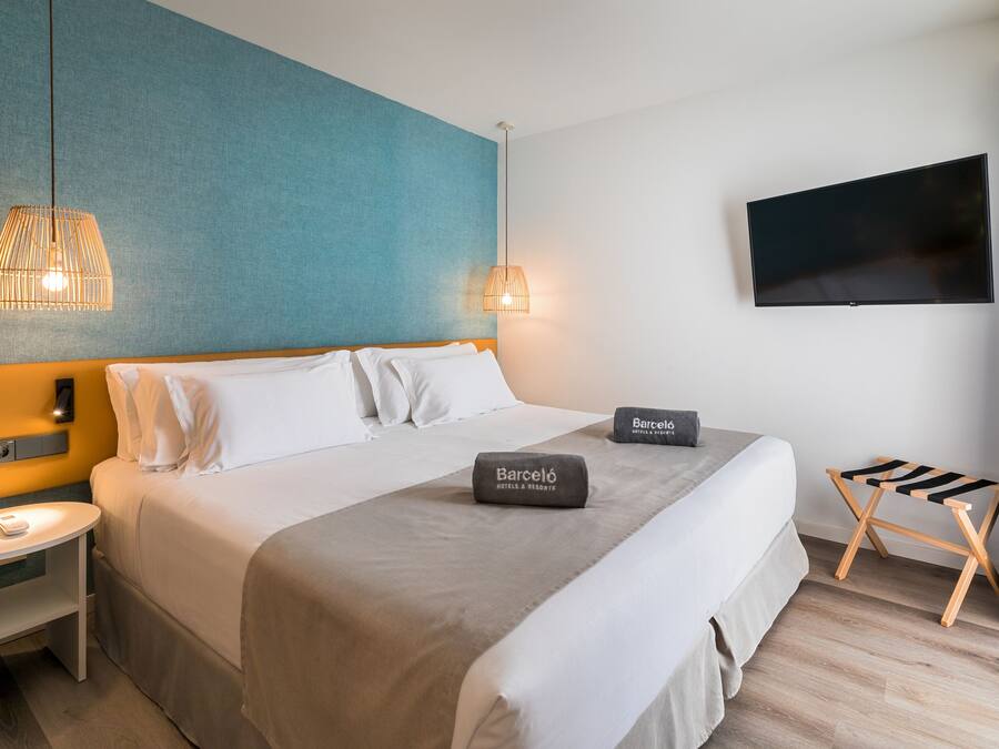 A hotel room with a bed, a nightstand, a TV, and a small table.