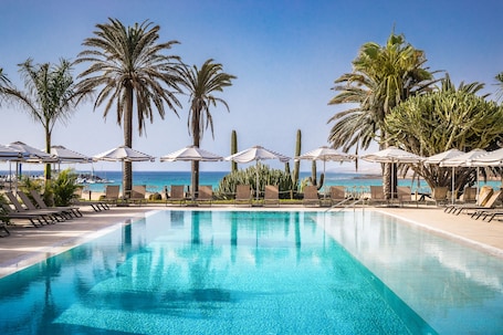 Una piscina al aire libre, sombrillas, sillones reclinables de piscina