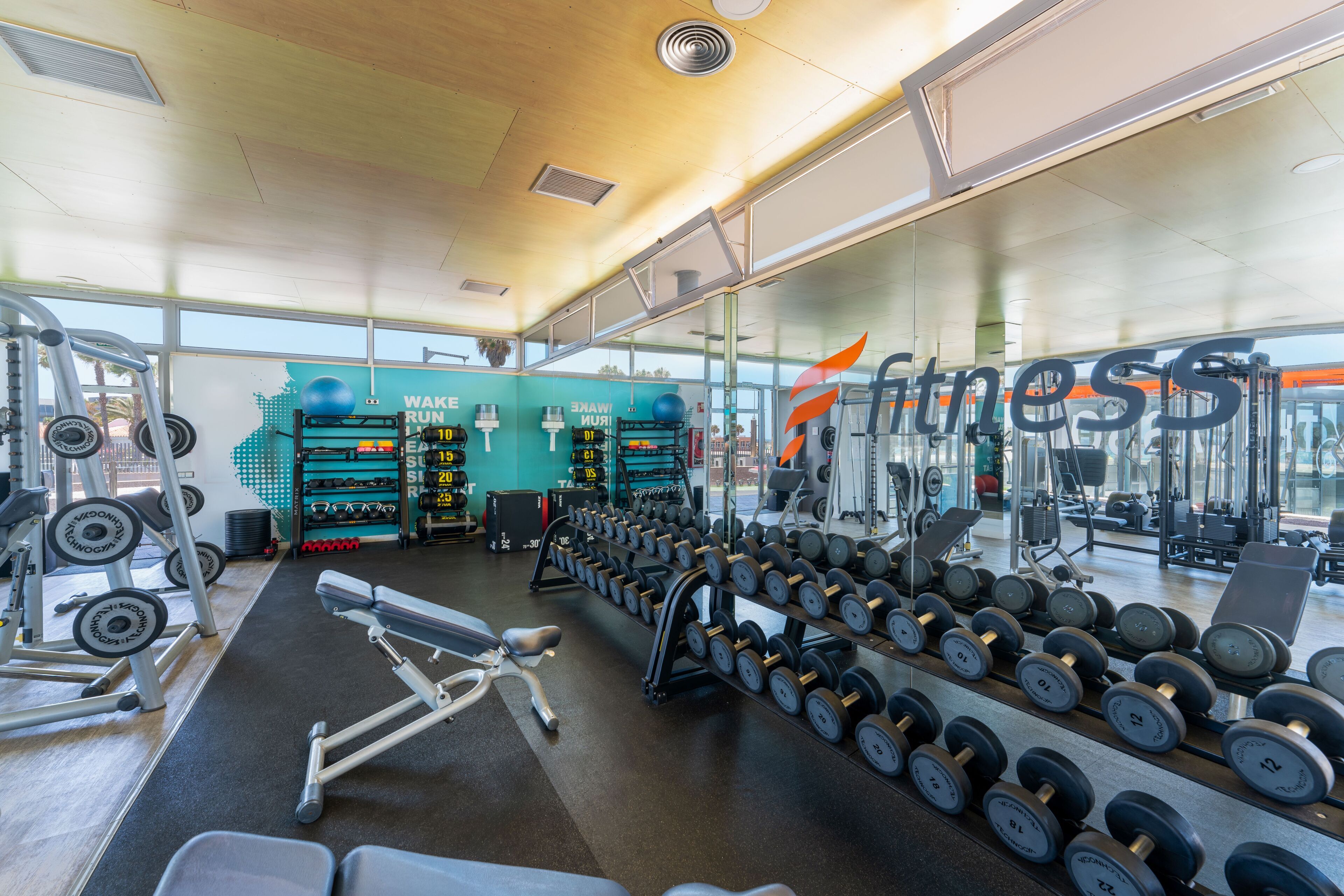 Uma academia com diversos equipamentos de exercício, incluindo halteres, máquinas de peso e equipamentos de cardio.