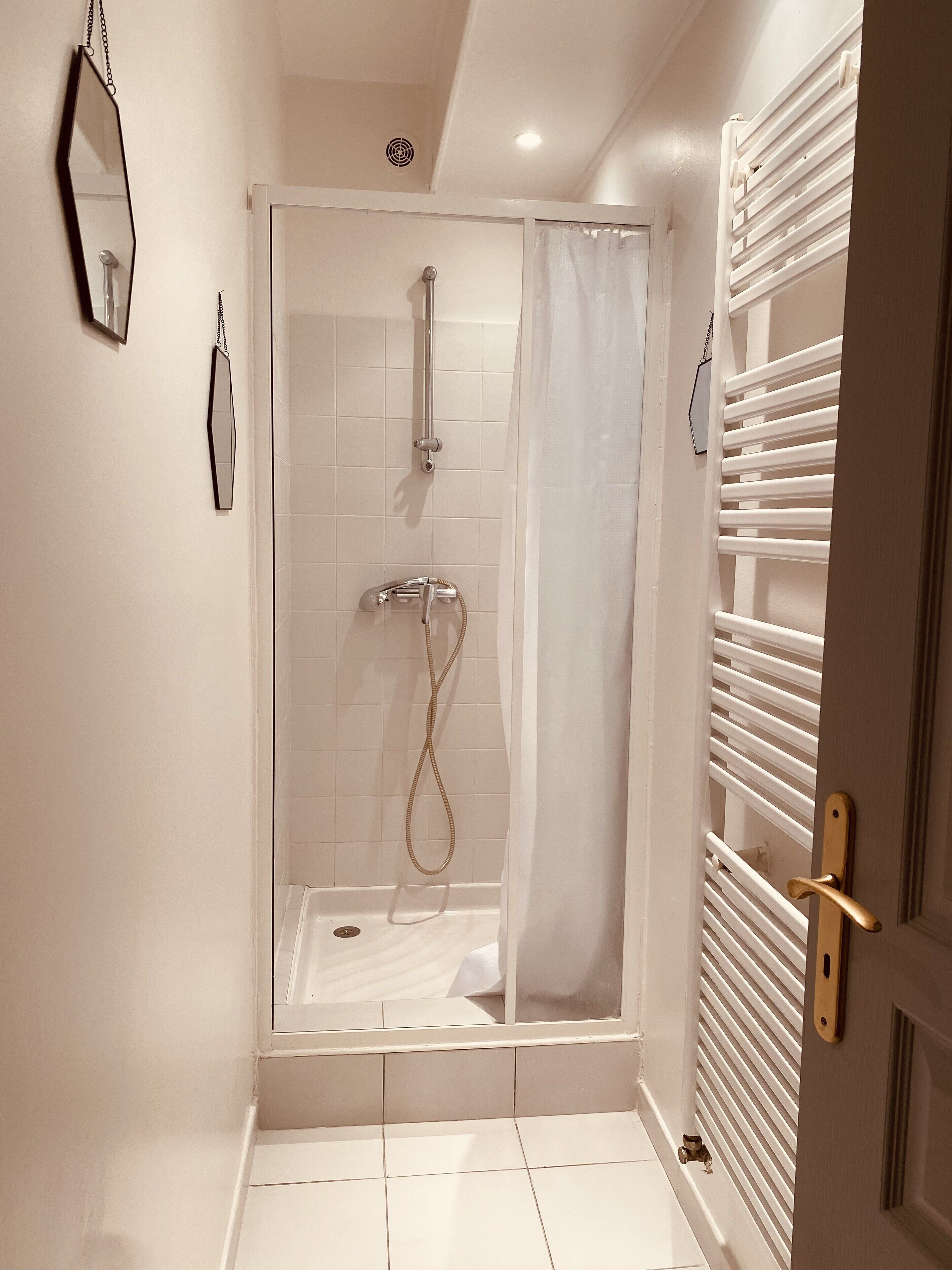Eine Dusche ohne trittfeste Duschwanne mit Glastür, weiß geflieste Böden und einem Handtuchhalter an der Wand.