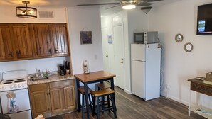 A compact kitchen with wooden cabinets, a white refrigerator, and a dining area with stools. - Little bit of Paradise (Corpus Christi)