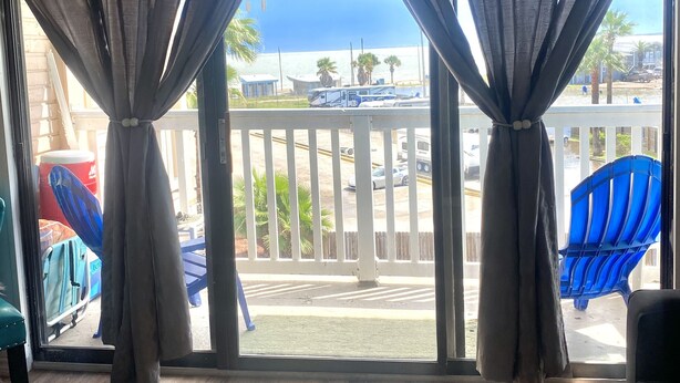 A room with a view of the beach, featuring a balcony with a railing and a blue chair. - Little bit of Paradise (Corpus Christi)