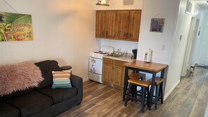 A compact living space with a kitchenette, a black sofa with a fluffy throw, and a wooden dining table with stools. - Little bit of Paradise (Corpus Christi)