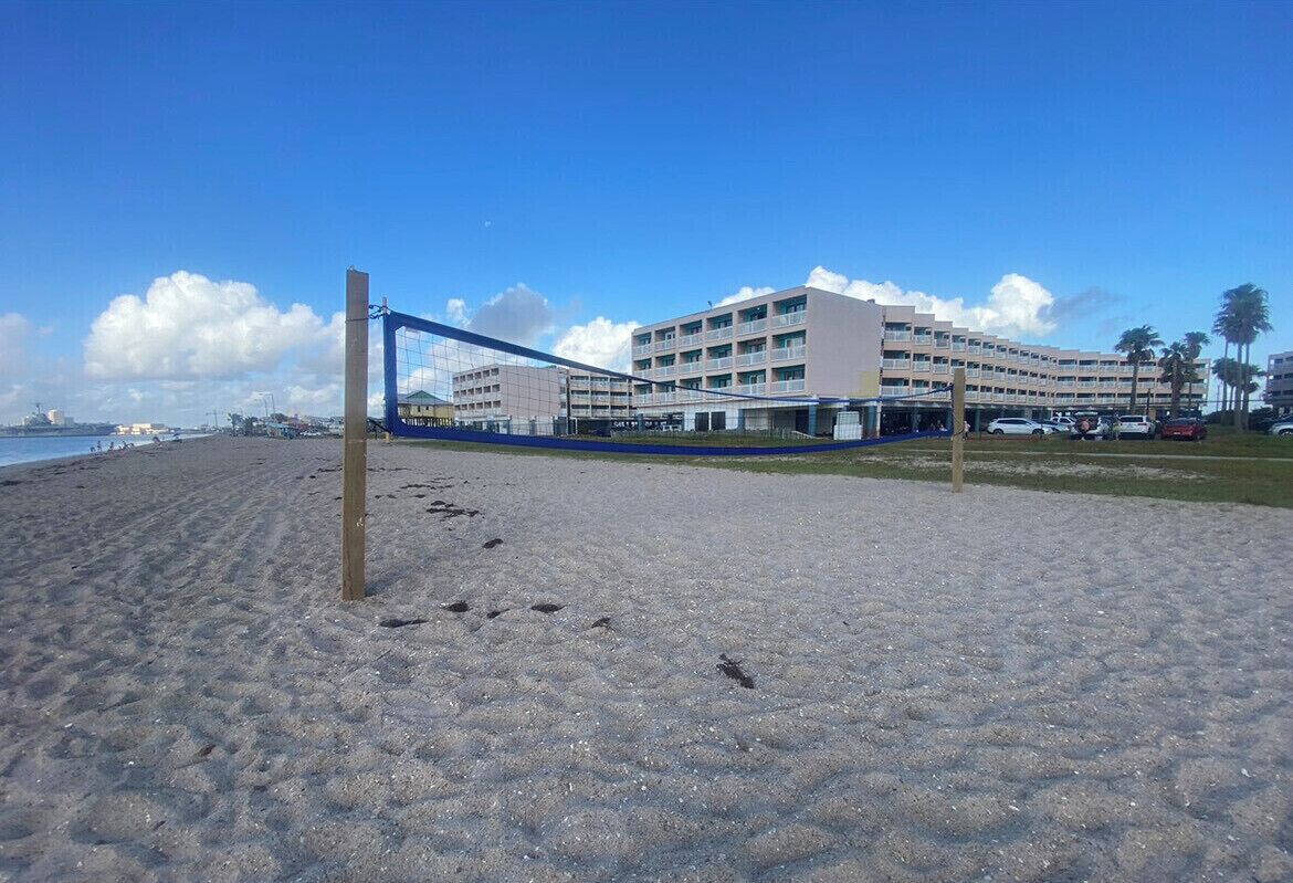 Une plage avec un filet de volley-ball, un immeuble à plusieurs étages et un ciel dégagé.