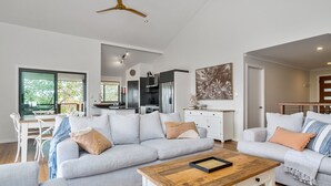 A modern living room with a grey sofa, a wooden coffee table, and a dining area with a white table and chairs. - Mulivista - spacious home with ocean views & pool (Suffolk Park)
