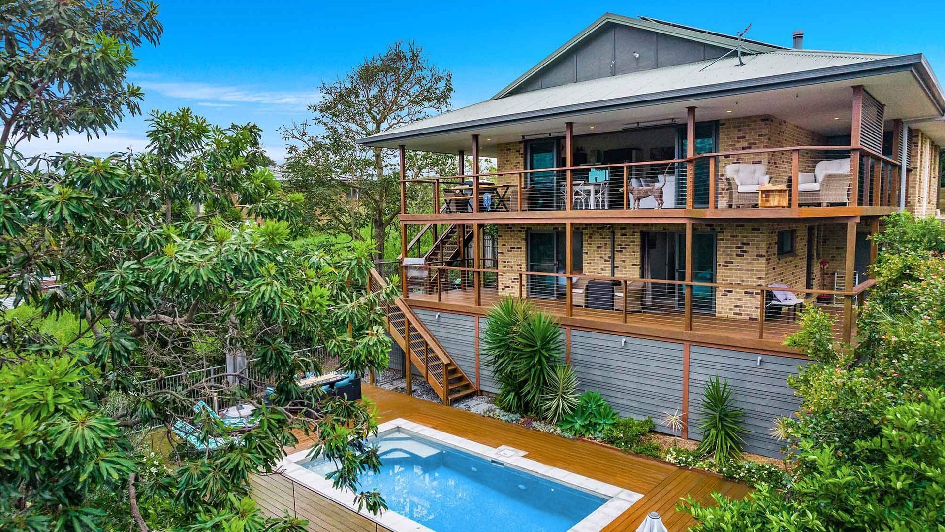 A two-story house with a balcony, a swimming pool, and lush greenery.