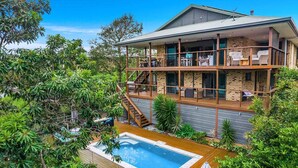 A two-story house with a balcony, a swimming pool, and lush greenery. - Mulivista - spacious home with ocean views & pool (Suffolk Park)