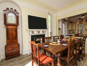 A dining room with a wooden table, chairs, a fireplace, and a large clock.