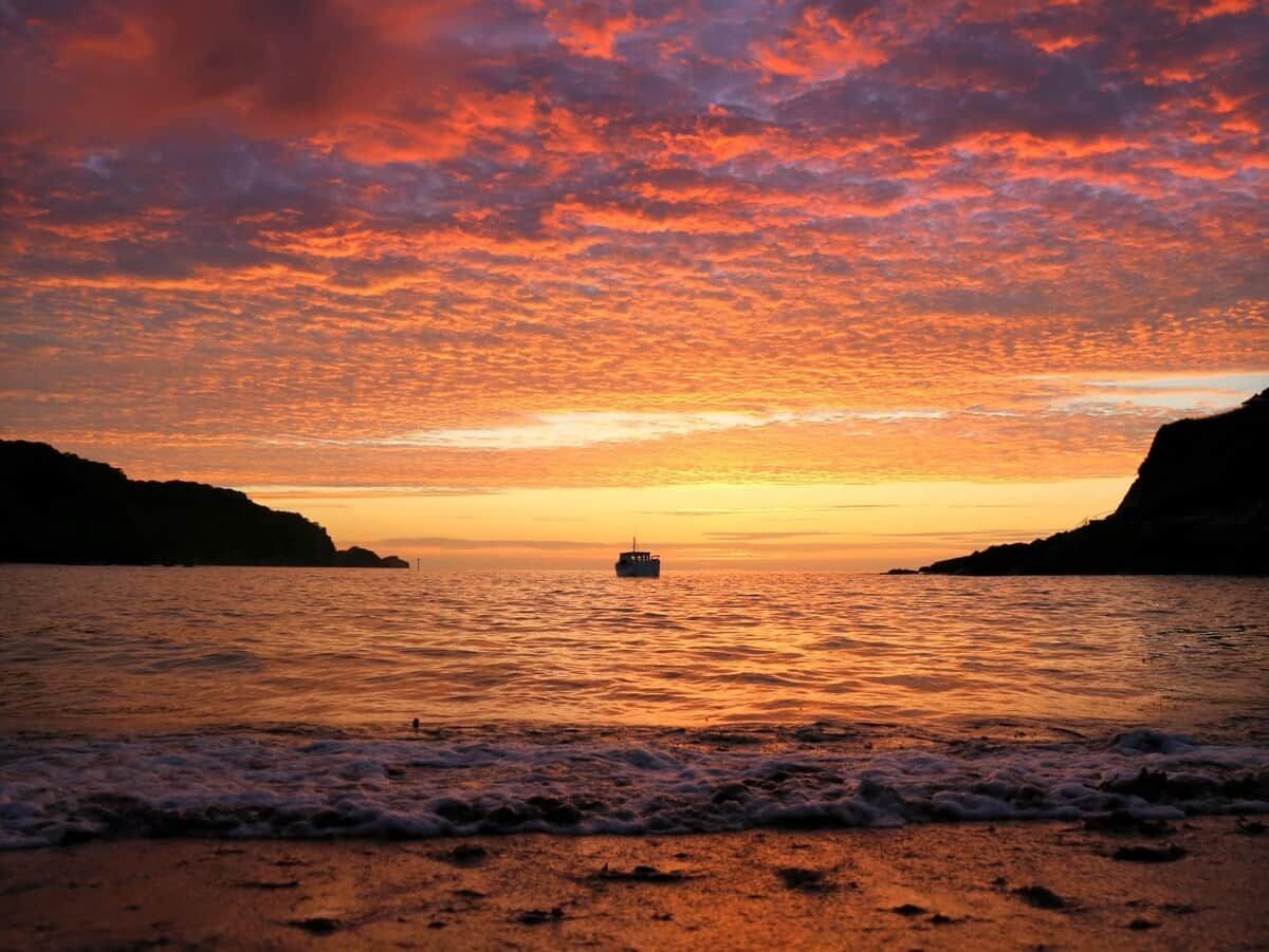 A sunset over a body of water with a boat in the center and cliffs on either side.
