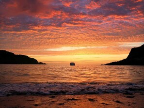 A sunset over a body of water with a boat in the center and cliffs on either side.