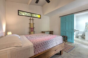 Une chambre à coucher avec un lit, une échelle, une petite table et une salle de bain avec des toilettes et une porte bleue.