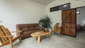 A living room with a brown leather sofa, wooden chairs, a coffee table, and a large potted plant. - Spacious 3BR Villa Just 5 Min Walk to the Beach | Master Suite & Saltwater Pool (Puerto Viejo de Talamanca)