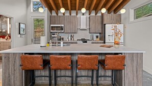 A modern kitchen with a large island, bar stools, and wooden ceiling beams.