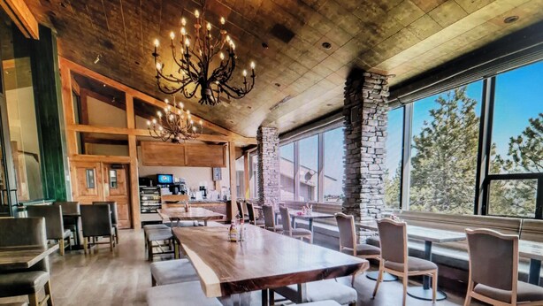 A spacious dining area with a long wooden table and benches, a chandelier, and large windows offering a view of the outdoors. - Experience Tahoe's Ski Scene at Holiday Inn Club Vacations Tahoe Ridge Resort (Stateline)