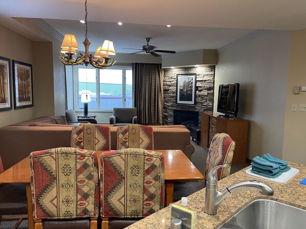 A modern living room with a stone fireplace, a dining area with patterned chairs, a television, and a ceiling fan. - Experience Tahoe's Ski Scene at Holiday Inn Club Vacations Tahoe Ridge Resort (Stateline)