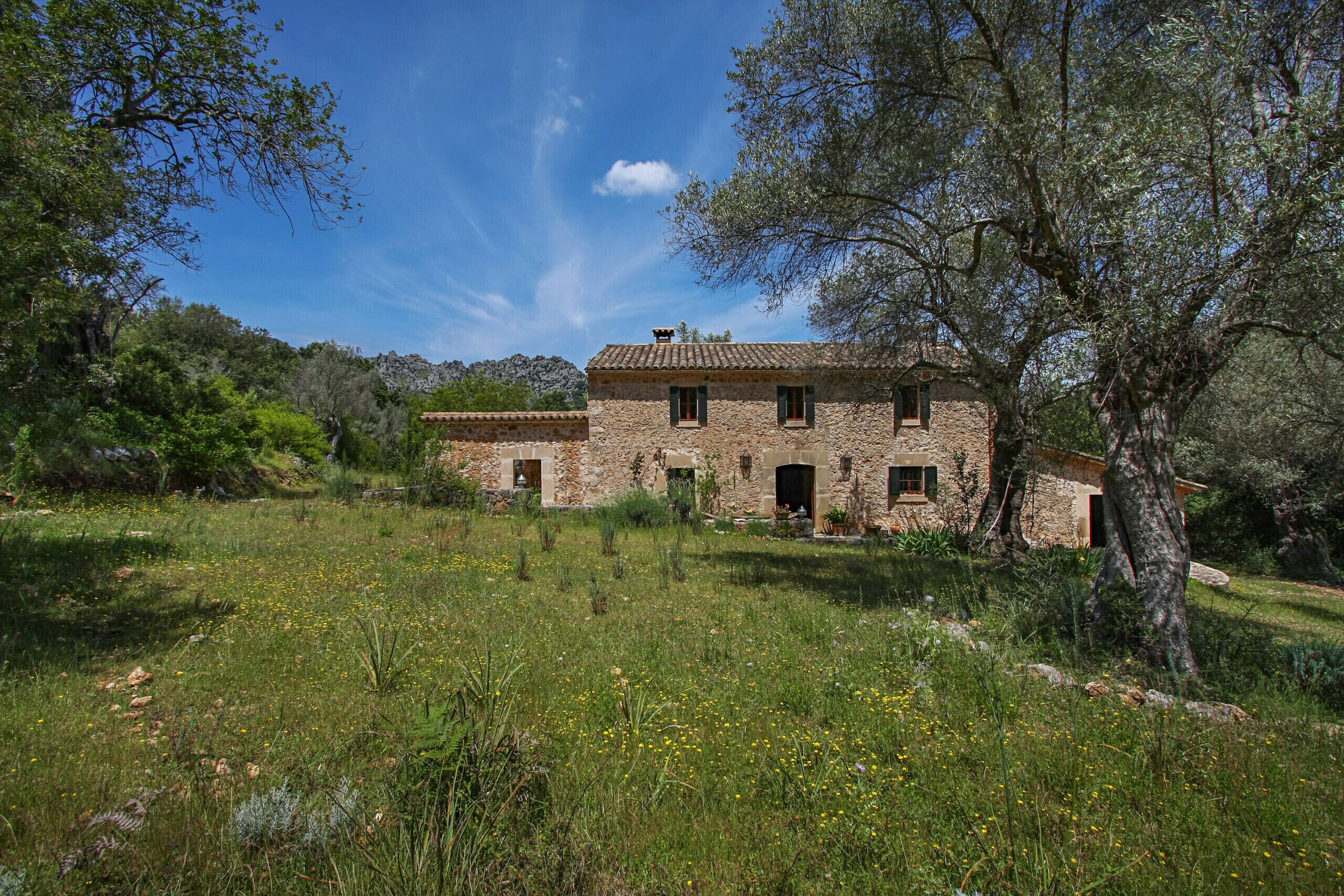 Uma casa de pedra com telhado de cerâmica, rodeada por um campo gramado e árvores.