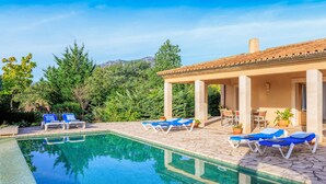 Una piscina con sillas de descanso, un porche cubierto y vistas a árboles y montañas.