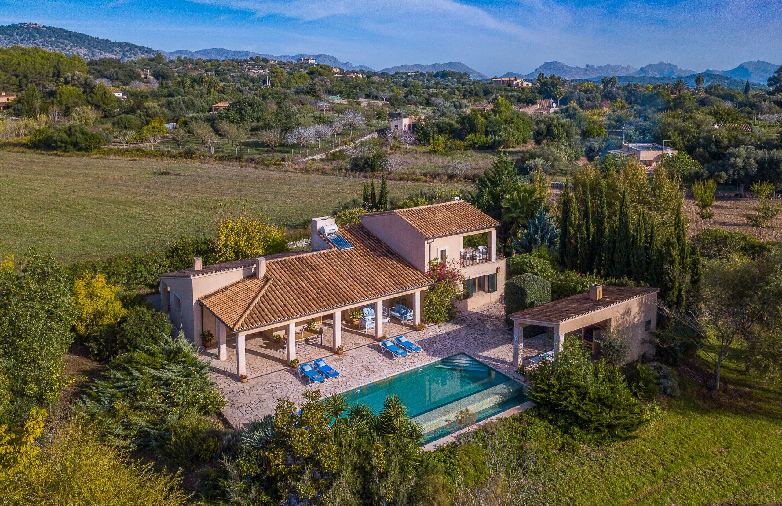 A villa with a swimming pool, outdoor seating, and a view of the surrounding countryside.