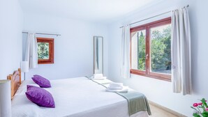 Un dormitorio con cama, ventana con cortinas, espejo y vista a zonas verdes.