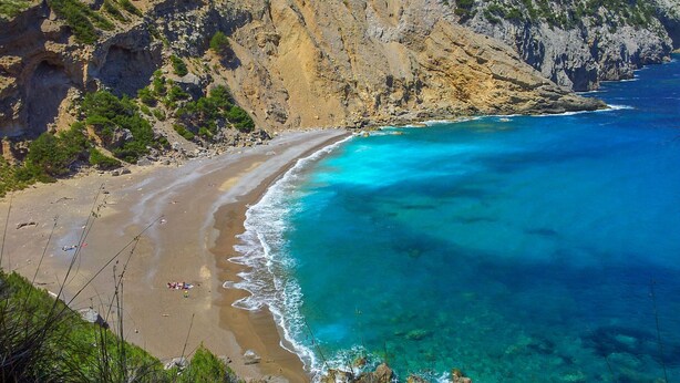 Un paisaje costero con una playa de arena, aguas turquesas cristalinas y acantilados rocosos.