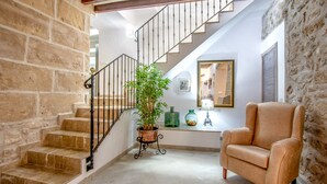 A staircase with a wrought iron railing, a potted plant, a green vase, and a beige armchair in a room with stone walls and a tiled floor. - Town55, House 5StarsHome Mallorca (Pollensa / Pollença)