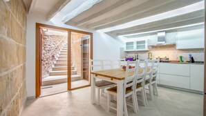 A modern kitchen with white cabinets, a wooden dining table, and a staircase leading to an upper level. - Town55, House 5StarsHome Mallorca (Pollensa / Pollença)
