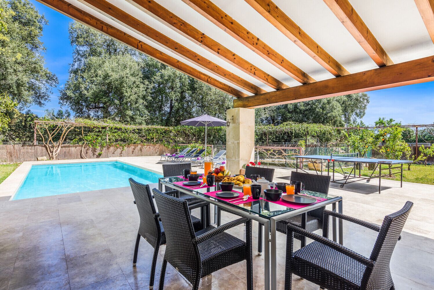 An outdoor patio with a pool, dining table, chairs, and a ping pong table.