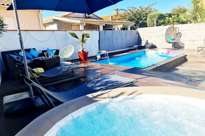 Un espace piscine comprenant un jacuzzi, des chaises longues et une petite table avec une bouteille d’eau.