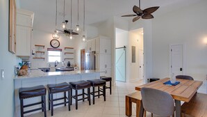 Uma cozinha moderna com uma ilha central, banquetas, uma mesa de jantar com cadeiras, luminárias pendentes e um ventilador de teto.