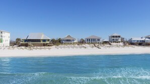 Um imóvel à beira-mar com várias casas ao longo da costa, uma praia de areia e o oceano.
