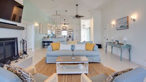 Uma sala de estar moderna com um sofá, mesa de centro e lareira. Cozinha e área de refeições podem ser vistas ao fundo.