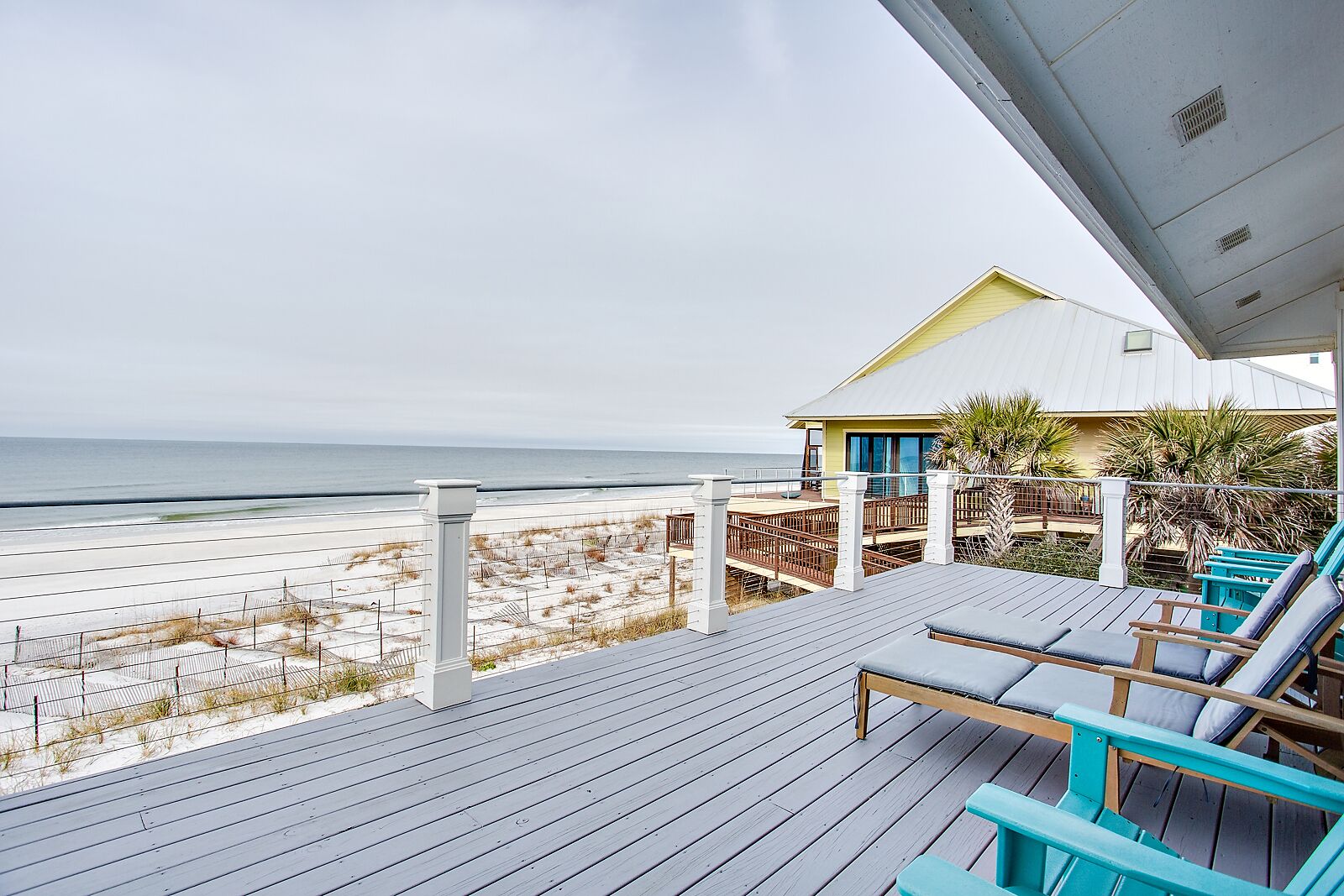 A beach house with a wooden deck, outdoor seating, and a view of the ocean.